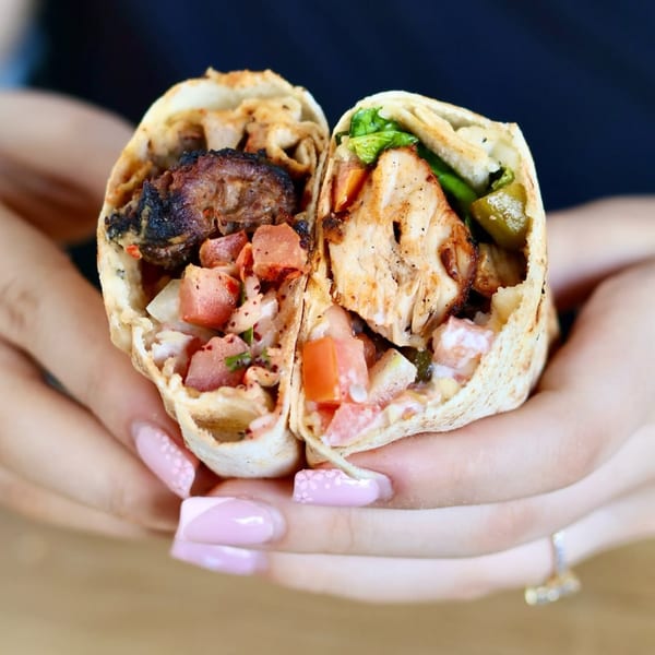 Hands holding two halves of a Mediterranean wrap, one with dark meat, the other with light meat.