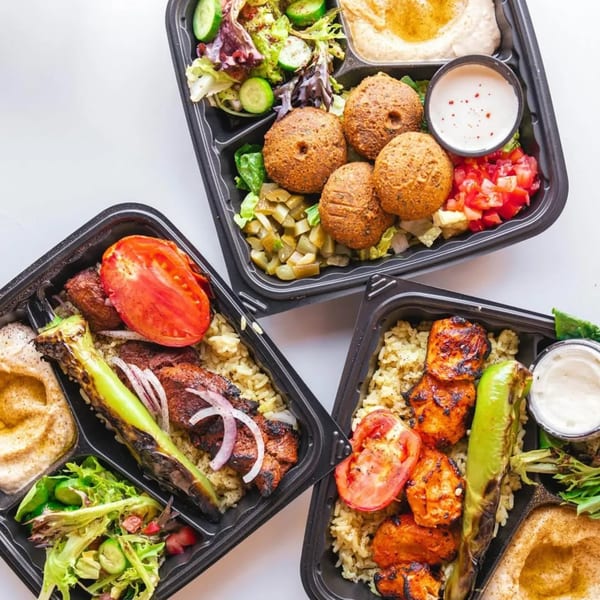 Three Wahib's Mediterranean Express takeout containers filled with falafel, chicken, and beef kebabs, rice, hummus, and salad.