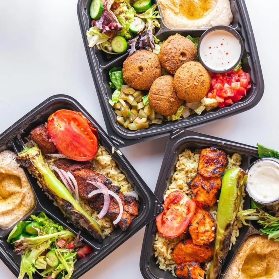 Three Wahib's Mediterranean Express takeout containers filled with falafel, chicken, and beef kebabs, rice, hummus, and salad.