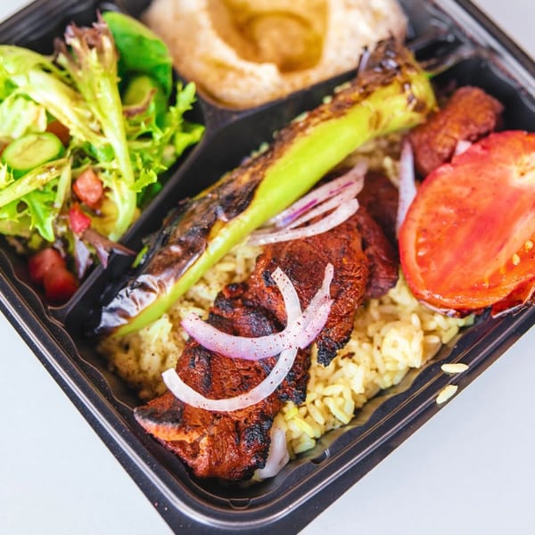 Wahib's Mediterranean Express meal with grilled chicken, rice, salad, hummus, and vegetables in a takeout container.