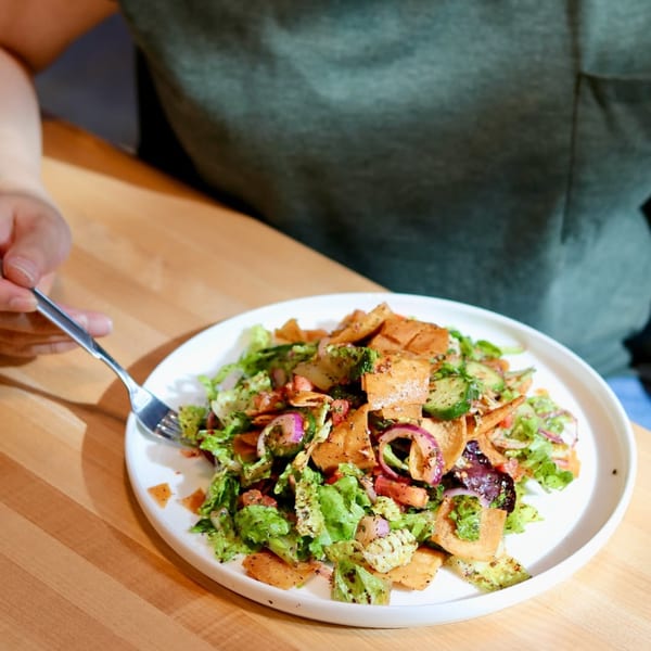 A person eating a fresh Wahib's Mediterranean Express Fattoush salad with a fork.
