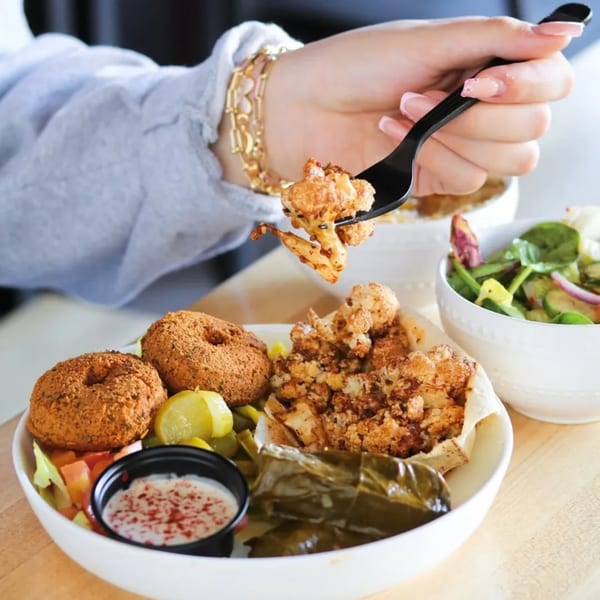 A person uses a fork to pick up a piece of fried cauliflower from a Mediterranean platter.